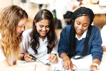 Poster - Three young women collaborating on an electronics project, smiling and engaged. Students study electrical circuit. Technological education. Students study electrical class together