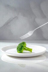 White fork hovering over single broccoli floret on minimalist white plate with gray background