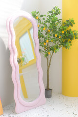 Aufkleber - pink wavy mirror stands beside potted plant in bright room. cheerful decor adds playful touch to space