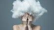 © olga_demina - Woman covering her face with her hands while a large white cloud covers her head, symbolizing stress, information overload, burnout, and mental health issues against a muted blue background
