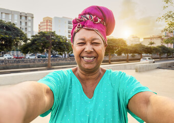 Wall Mural - Happy african senior woman taking selfie while wearing traditional clothes - Joyful elderly lifestyle and travel vacation concept - Focus on face