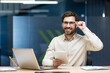 © Tetiana - Portrait of a young smiling man working in the office, sitting at a desk with a laptop, holding glasses, using a tablet and looking at the camera