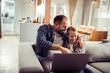 © Geber86 - Father and daughter using a laptop while sitting on the couch in the living room