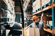 © Davor - Smiling male worker using smartphone and carrying box in large warehouse