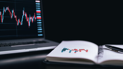 Poster - laptop displaying stock market data alongside a notebook with financial charts and a pen. the scene 