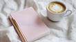 © Susan - A pink notebook with a gold pen rests beside a cup of latte art coffee on a white bedsheet.  Perfect morning scene!