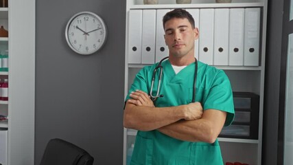 Wall Mural - Male doctor standing confidently in a hospital room with arms crossed wearing green scrubs and stethoscope around his neck signifying professionalism and healthcare environment.