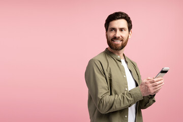 Wall Mural - Handsome young man with smartphone looking away on copy space on pink background