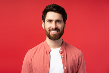 Wall Mural - Happy bearded Hispanic young man in casual looking at camera, isolated on red