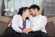 © charnsitr - Couple sharing a joyful moment while sitting closely together on a couch in a living room