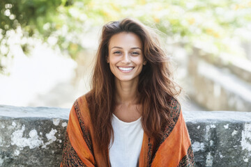 Young woman with long hair smiling warmly outdoors wrapped in a shawl during daytime