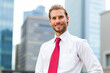 © Minerva Studio - Smiling businessman standing in front of skyscrapers in business district
