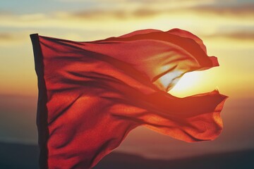 Poster - A red flag being blown by the wind at sunset, with a warm orange glow