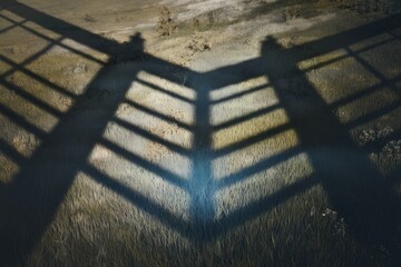 Aufkleber - V-shaped shadow of a gate on grassy ground, creating a symmetrical and intriguing pattern.