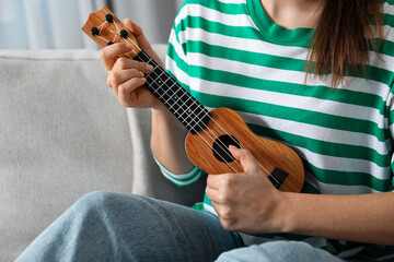 Wall Mural - Woman playing ukulele on sofa at home, closeup