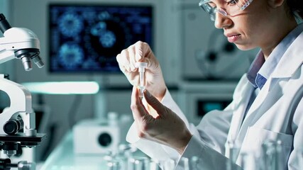Poster - Female scientist wearing lab coat and protective glasses carefully examines a sample in a test tube in a modern laboratory setting, captured in slow motion
