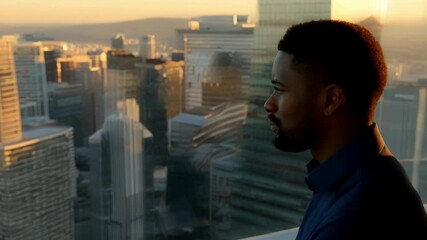 Poster - Young businessman looking out of skyscraper window at sunset over modern city with contemplative expression, enjoying the view and reflecting on his success
