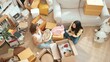 © InfiniteFlow - Top view of happy friend unpacking box and picking furniture together. Attractive teenager moving to new apartment while plating talking at living room surrounded with cardboard box. Estate. Myrmidon.