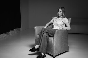 black and white photo, young, emotional, business girl sitting on a leather chair, wearing a white t-shirt, stress, worries, looking straight ahead. Modern minimalist portrait of business or life them