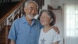 © sukarman - portrait of an asian elderly couple standing in a room with a staircase in the background. The asian man is on the left side of the image