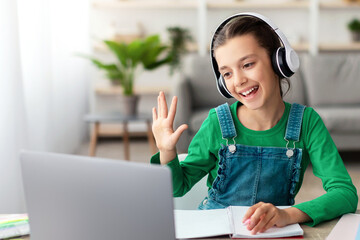 Poster - Online Video Call And Communication. Portrait of cheerful teenage pupil sitting at table, using laptop having virtual conference, waving hand to webcam greeting teacher and classmates, writing