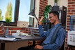 © DC Studio - Young male employee wearing wireless earphones waves at his laptop during an online conversation. African american manager starts virtual meeting on device, greeting clients on videocall with a smile.