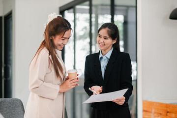 Wall Mural - Two businesswomen engaged in a friendly discussion, sharing documents and ideas in a contemporary office environment.