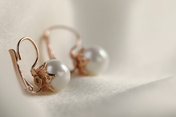 Wall Mural - Beautiful pearl earrings on white silk, closeup. Space for text