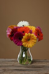 Wall Mural - Bouquet of beautiful gerbera flowers in glass vase on wooden table against brown background