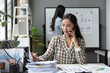© amnaj - Businesswoman talking on phone and analyzing financial charts in office