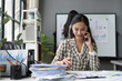 © amnaj - Smiling businesswoman talking on mobile phone and checking documents at office desk