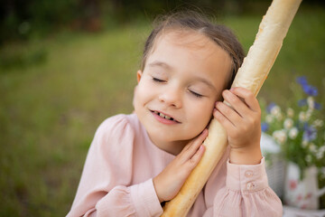 Wall Mural - A gentle summer picnic by the water. Portrait of a blue-eyed girl with long hair in a light dress on the grass and on a beige blanket with flower and fruit. A gentle rest. Warm evening