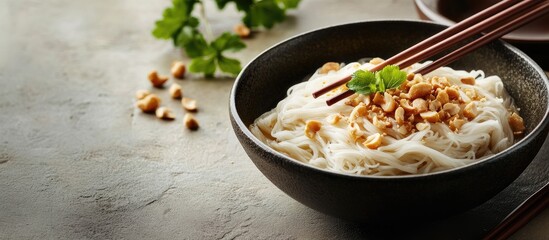 Poster - Delicious bowl of rice noodles topped with crushed peanuts and fresh cilantro on a textured gray surface with chopsticks resting on the side