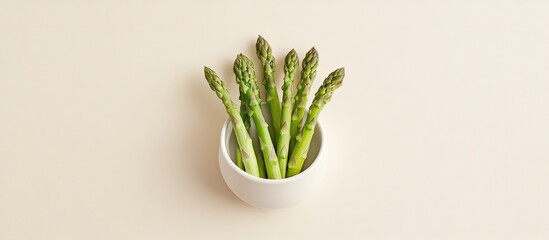 Poster - Fresh green asparagus tips elegantly placed in a white bowl against a soft cream background, showcasing vibrant color contrast in flat lay style.