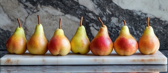 Poster - Vibrant fresh pears in shades of green and red neatly arranged on a white marble cutting board against a rich, textured marble backdrop.