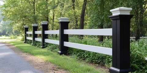 Sticker - Elegant black and white wooden fence surrounded by lush green foliage along a peaceful country road with vibrant trees in the background.