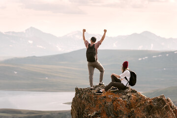 Fototapete - Couple of young happy hikers or tourists are relaxing at mountain top with great view at lakes and high mountains