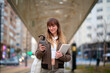 © Cavan Images - Woman engages with phone while holding book at urban location