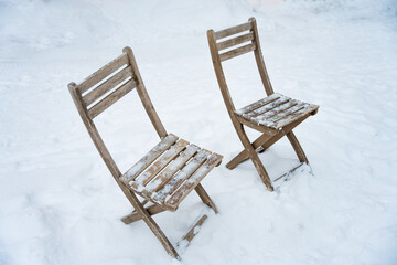 Two rustic wooden chairs partially covered with snow stand abandoned in a quiet winter setting