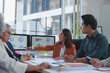 © crizzystudio - Businesswoman pointing at charts on a computer screen while leading a discussion during a meeting with colleagues in a modern office environment, fostering teamwork and collaboration