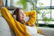 © Yingyaipumi - Happy young asian woman use headphones and relaxing at home.Female smile sitting on sofa,couch and holding mobile smartphone.Listening to music on lazy and radiating joy and relaxation.