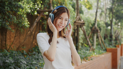 Wall Mural - Attractive Enjoying music outdoors, woman smiles while ing headphones in lush garden setting. vibrant greenery enhances joyful atmosphere. Asian Woman Lifestyle