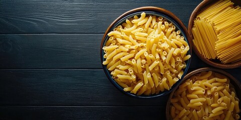 Aufkleber - Stylish top view of macaroni and spaghetti in deep blue and wooden bowls with bright yellow pasta on dark wooden surface for culinary inspiration