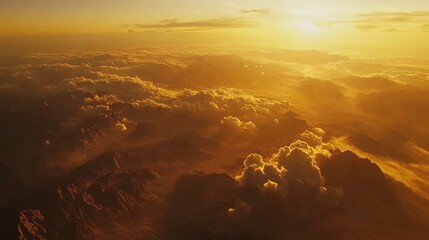 Poster - A stunning aerial shot of vast mountains bathed in the warm golden light of a sunset, clouds floating over the terrain from an airplane window.