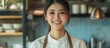 © CreativeBro - Smiling Asian female chef in modern kitchen with apron ready to serve culinary delights and provide empty space for promotional text