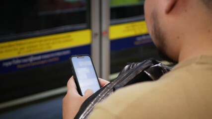 Canvas Print - close up to hand of asian young man use 5g smartphone mobile phone in the subway station while waiting for arrival upcoming subway train. Asian man passenger in public transportation background