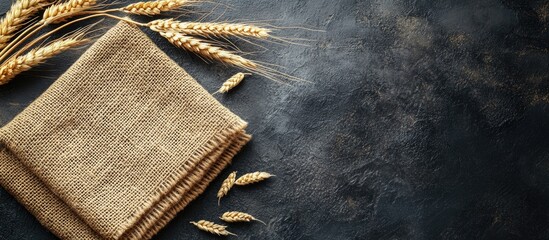 Poster - Burlap napkin with ears of wheat on a dark textured background top view with ample copyspace for rustic design or food related content