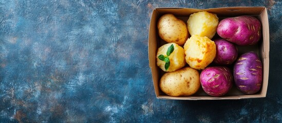 Poster - Vibrant assortment of purple and yellow potatoes in a cardboard container with space for text showcasing fresh seasonal produce.