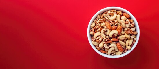 Poster - Bowl of Mixed Nuts Including Almonds Cashews Walnuts and Pecans on Vibrant Red Background with Room for Text or Copy Space