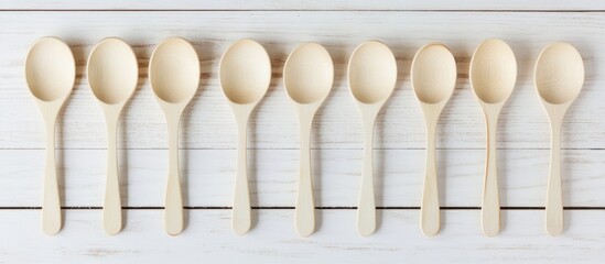 Poster - Design concept of empty wooden spoons lined up on a white wooden background with ample copy space for branding or product placement